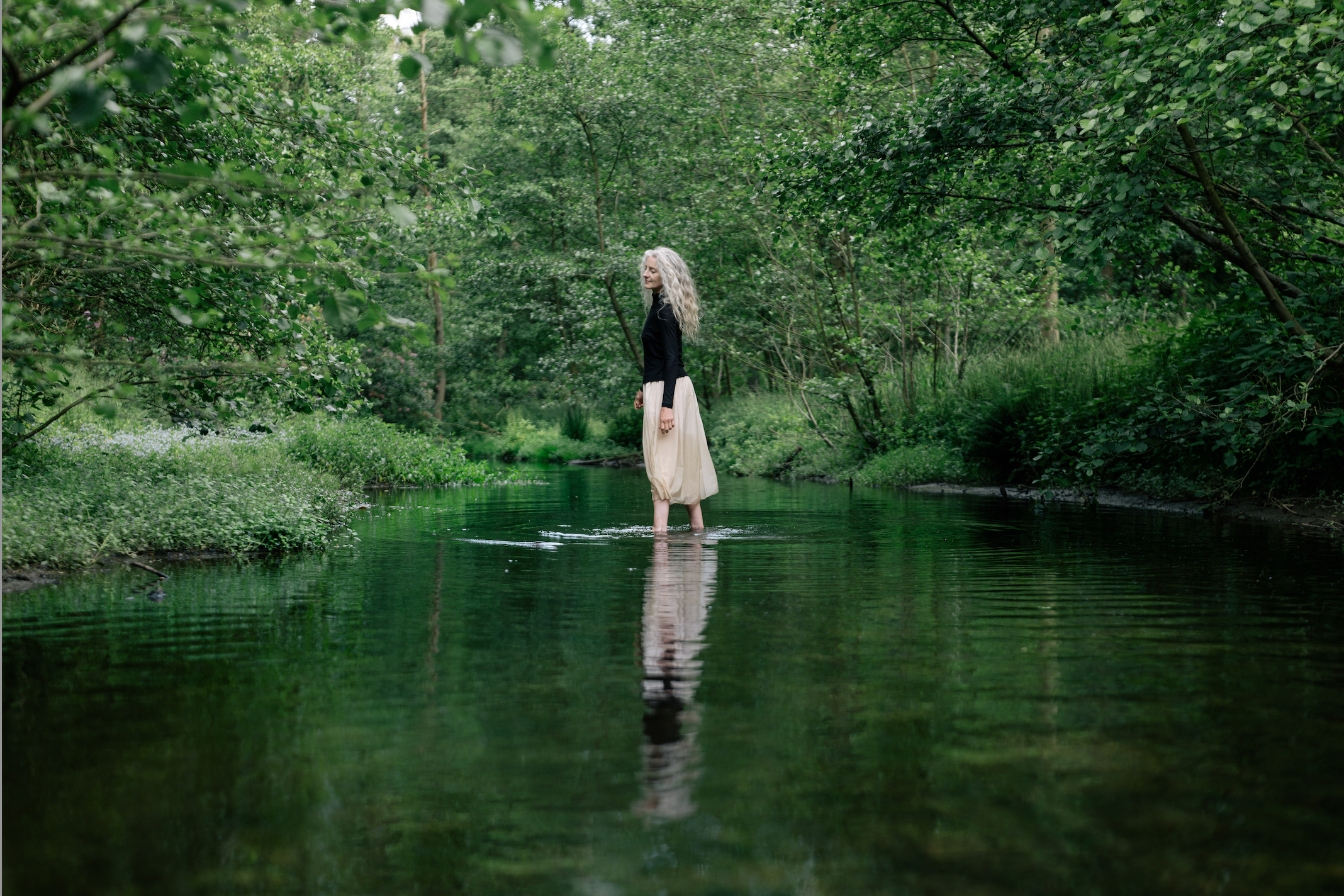 Eine Frau steht in seichtem Gewässer in einer Lichtung eines Waldes